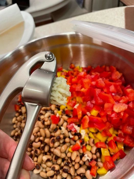 Pressed garlic over a bowl of black-eyed peas and diced bell peppers, likely prepping for a delicious dish.