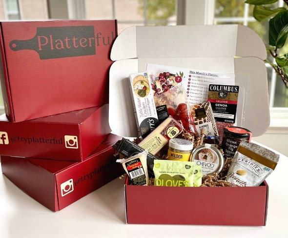 A large Platterful subscription box showcasing an array of gourmet snacks, such as cheese, salami, olives, and crackers.