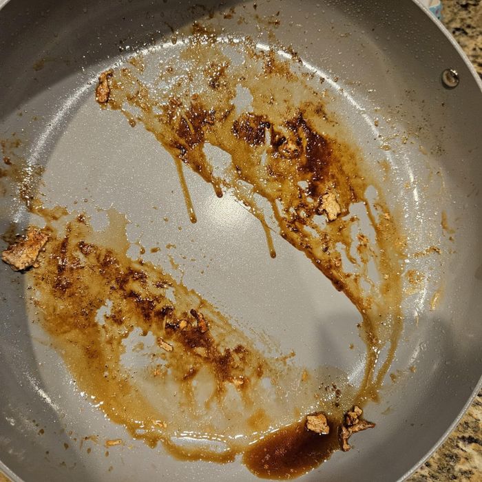 A large frying pan with leftover grease and food remnants after cooking, with a clean streak showing the effectiveness of the Powerwash.