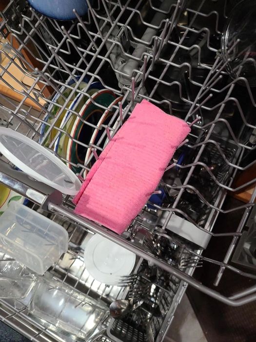Dishwasher filled with various dishes, and a pink cloth hanging on the upper rack.
