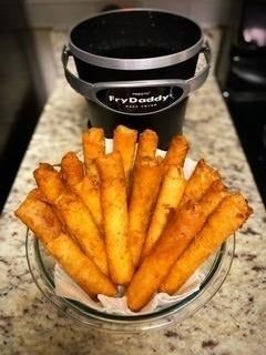 A bowl of golden, crispy fries sits in front of a FryDaddy deep fryer