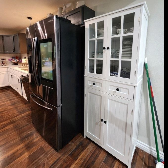 A modern kitchen featuring a sleek stainless steel fridge and crisp white cabinetry, including a tall storage cupboard.