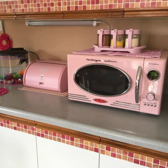 A set of retro-style pink kitchen appliances, featuring a pink microwave and bread bin, arranged neatly on a countertop