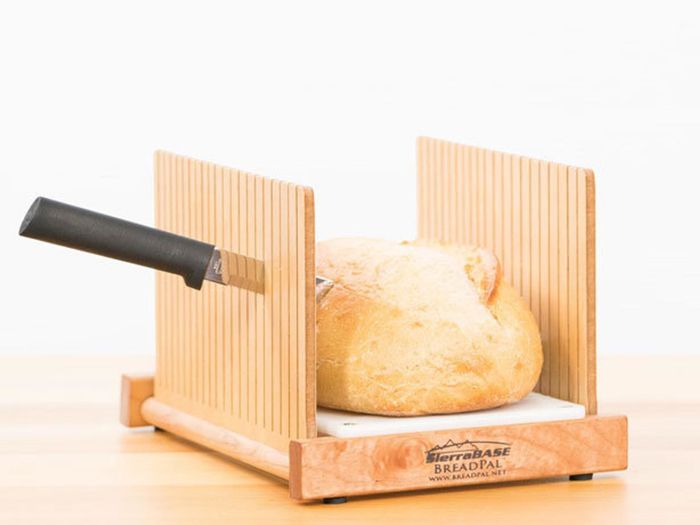 The wooden bread slicer with a knife cutting through a loaf between the slats.