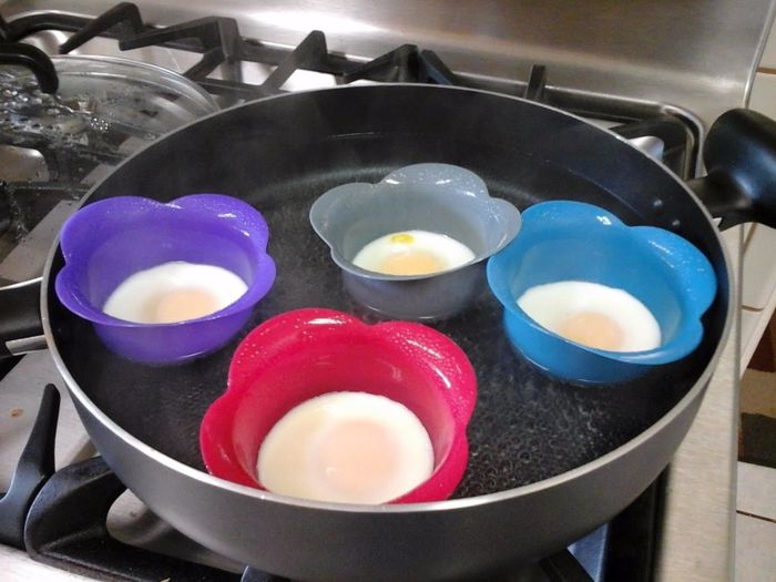 The four poached eggs in their silicone cups, gently cooking in a pan of hot water.