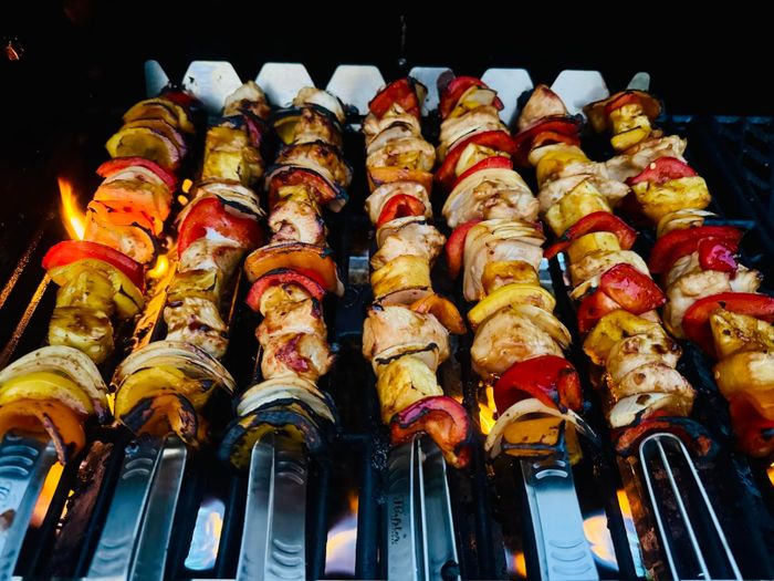 A variety of grilled vegetable kebabs with onions, bell peppers, mushrooms, and zucchini sizzling on a barbecue grill, flames dancing beneath them