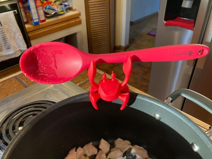 A crab-shaped silicone utensil holder perched on the edge of a pot