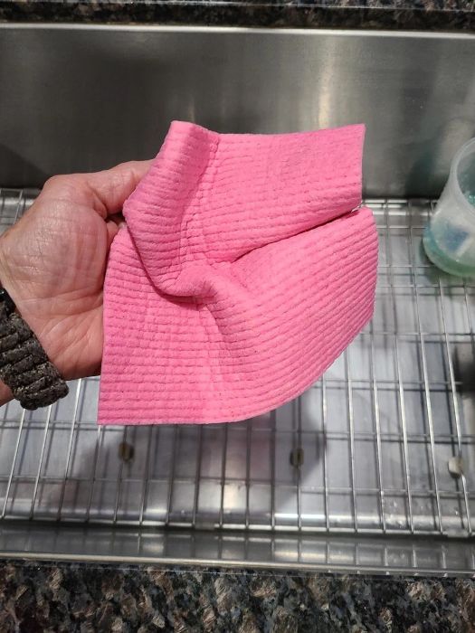 A hand holding a pink textured kitchen towel with a twist design.