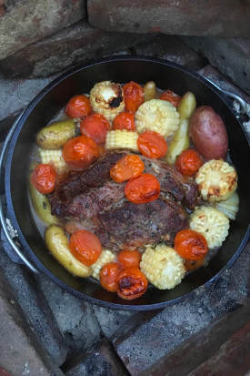 A review image showing a Dutch oven filled with meat, corn, potatoes, and assorted vegetables cooking to perfection