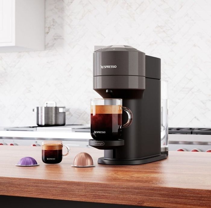 An espresso machine placed on a kitchen counter, with a cup of coffee and capsules next to it.
