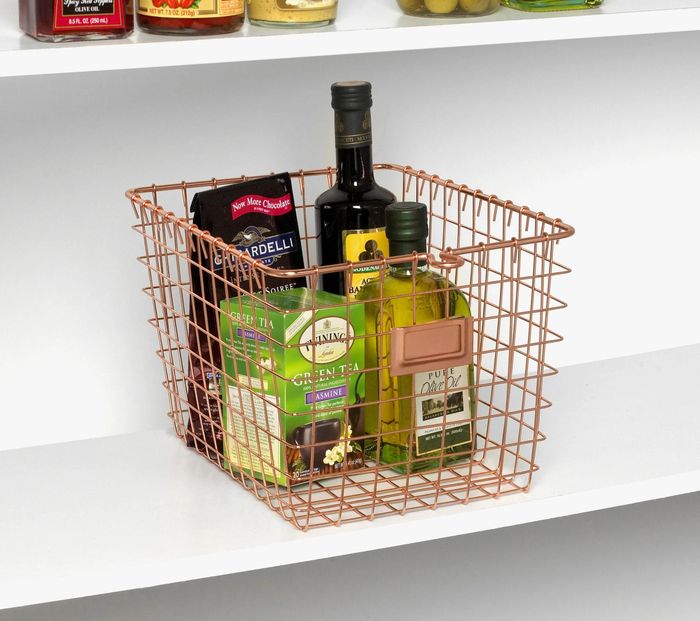 A rose gold wire basket filled with chocolate, tea, and olive oil, creating an elegant and organized display