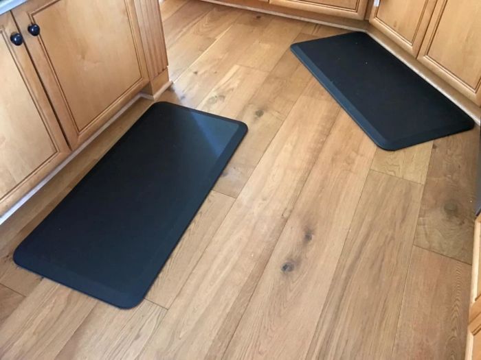 Two anti-fatigue mats laid on a wooden floor in a kitchen setting