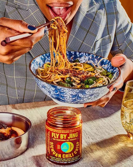 model enjoying noodles with a jar of chili crisp placed on the table