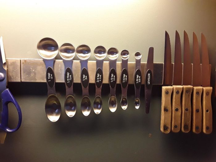 A set of measuring spoons attached to a magnetic strip mounted on the wall.