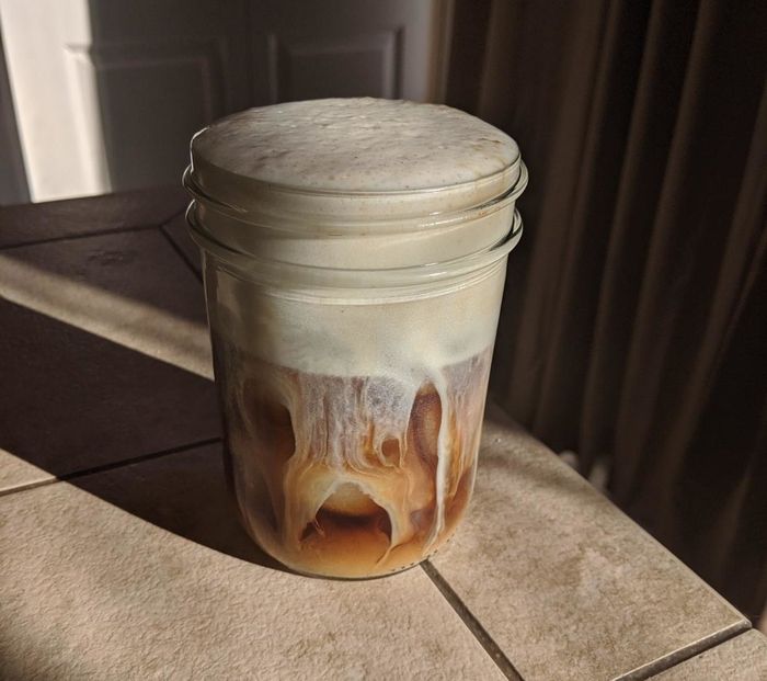 A mason jar filled with iced coffee topped with a thick layer of foam.