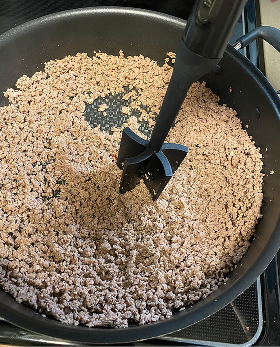 A reviewer holding a spatula above a pan of ground meat