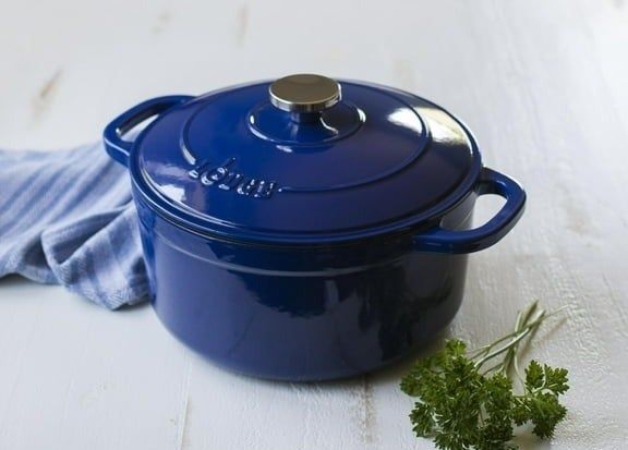 A blue enamel cast-iron pot resting on a white wooden surface, with a sprig of fresh parsley nearby