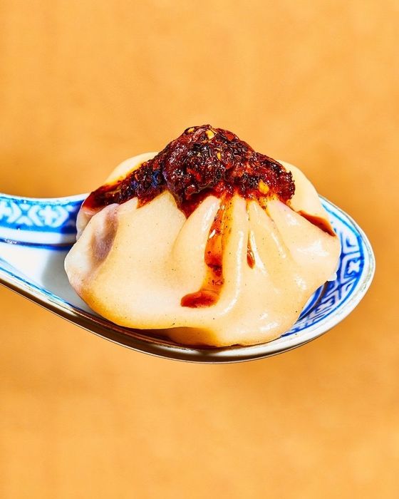 A soup dumpling garnished with chili crisp on a spoon
