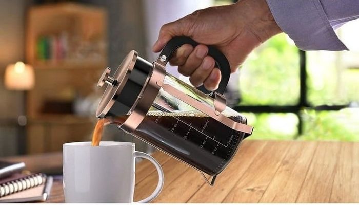 A person pouring coffee from a French press into a cup