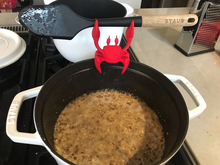 Reviewer's spoon held above a cast iron Dutch oven with a red crab spoon holder