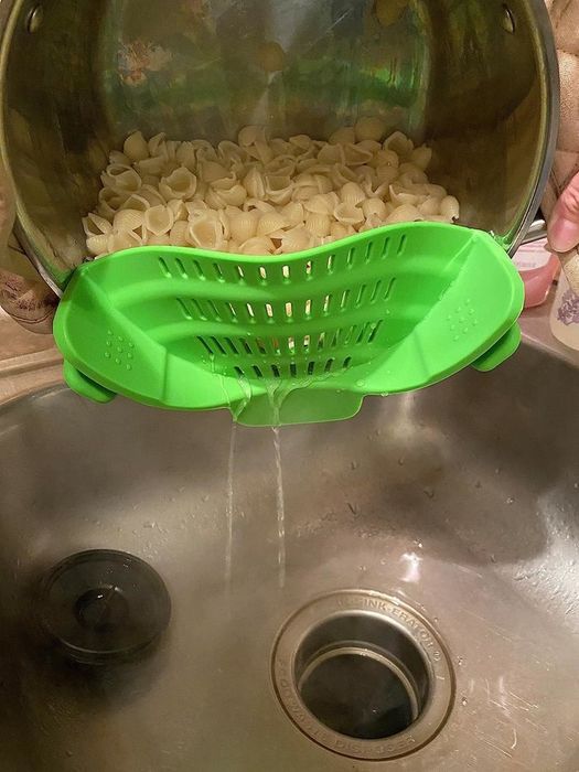 Reviewer using a green clip-on strainer to drain water from a pot of shell pasta noodles