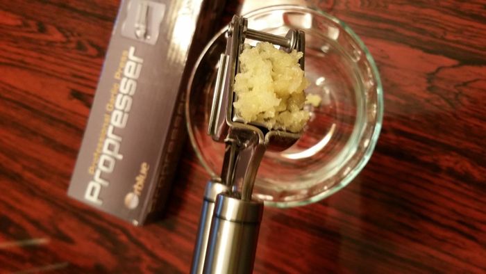 A reviewer demonstrates the use of the handheld garlic press, producing a smooth, thick garlic paste.