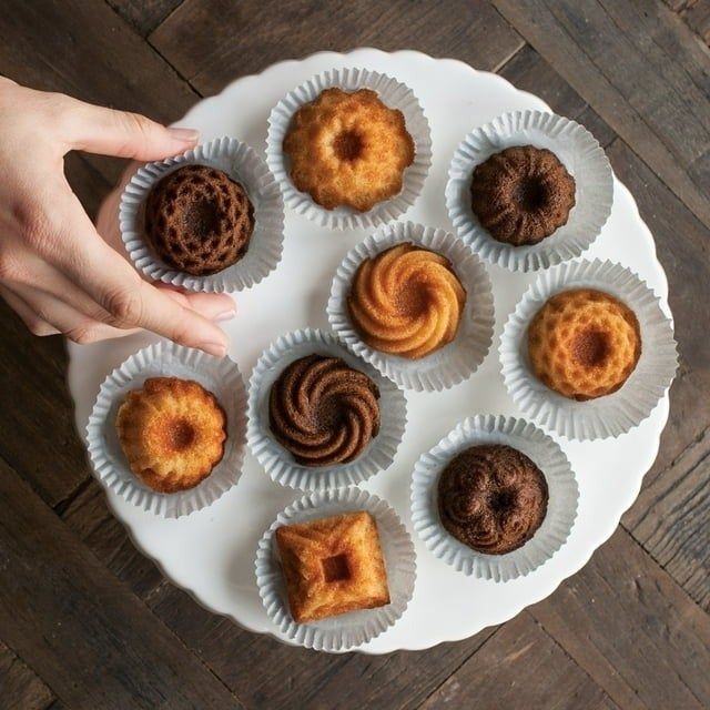 A hand selects a pastry from a platter of assorted mini bundt cakes