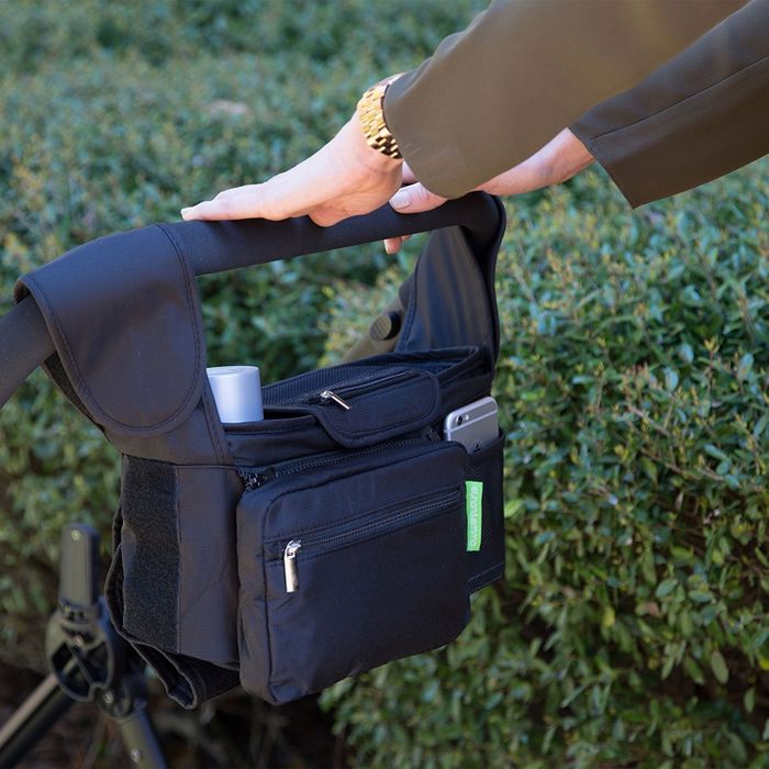 A person pushing a stroller with a storage bag hanging from the handle