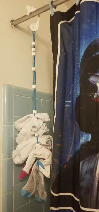 A hanging laundry organizer with socks tucked behind a shower curtain, featuring a space theme in a bathroom setting