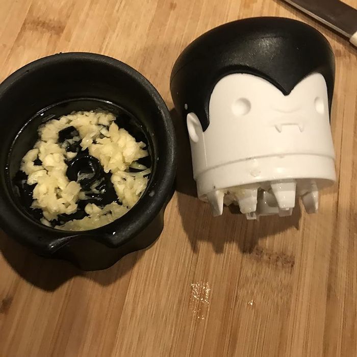 A Dracula-shaped garlic crusher in action, with crushed garlic pieces emerging through the holes, resembling spiky hair