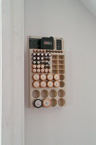 A wall-mounted battery organizer neatly holding different sizes of batteries, including AA, AAA, and C cells, with a convenient battery tester positioned at the top.
