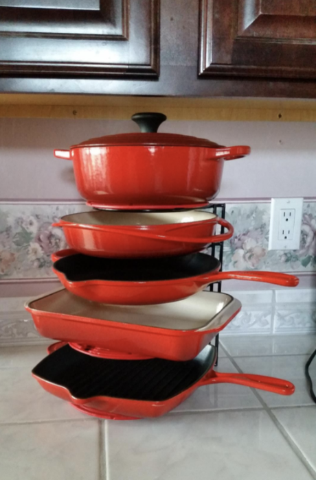 A vertical organizer holding five pieces of red Le Creuset cast iron cookware.