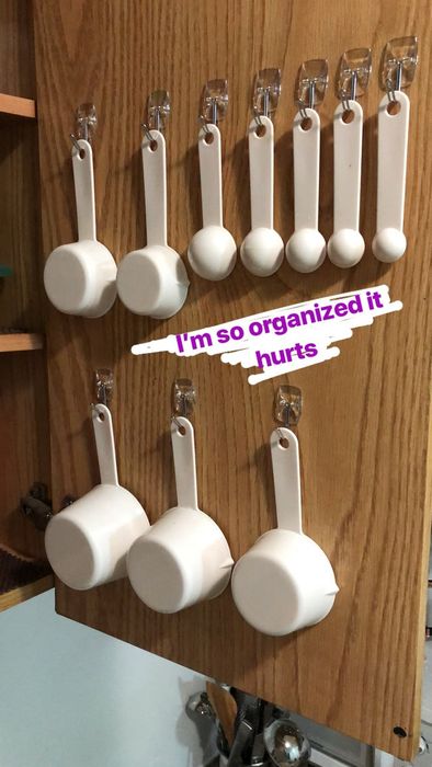 Writer's photo of the inside of a kitchen cabinet, featuring mounted Command hooks holding measuring cups and spoons