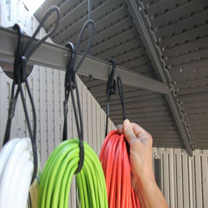 A person using a bungee cord to hang a coiled extension cord neatly