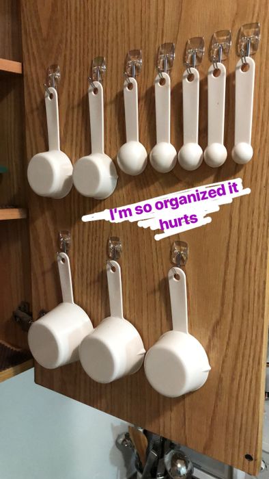A photo of a kitchen cabinet interior with Command hooks mounted, holding measuring cups and spoons