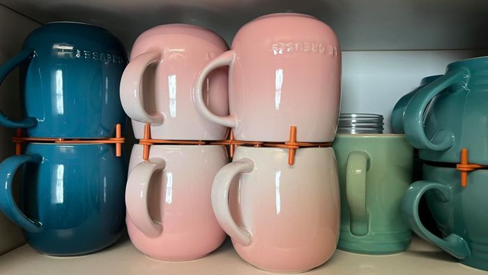Stacked ceramic mugs with spacers on a shelf for organized kitchen storage