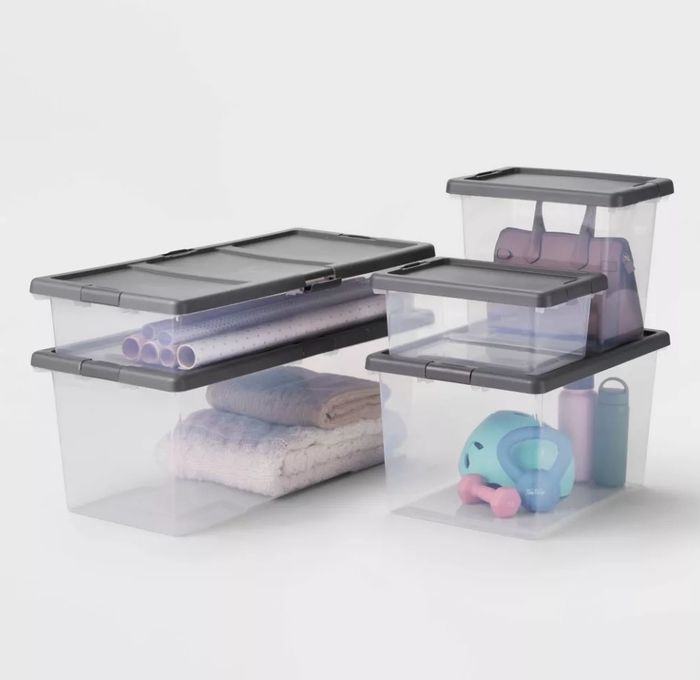 Stacked plastic storage containers neatly holding various household items, including rolled towels, toys, and a yoga mat, all organized in one place.