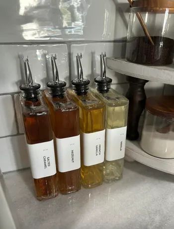 Four glass bottles labeled Salted Caramel, Hazelnut, French Vanilla, and Vanilla, arranged on a marble countertop next to jars of sugar and coffee