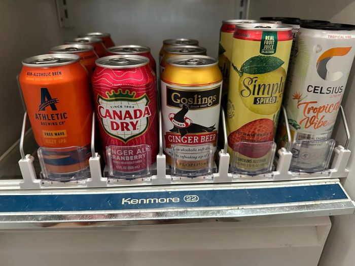 A variety of beverage cans on a refrigerator shelf, including Athletic Brewing Co., Canada Dry, Goslings, Simply Spiked, and Celsius Tropical Vibe