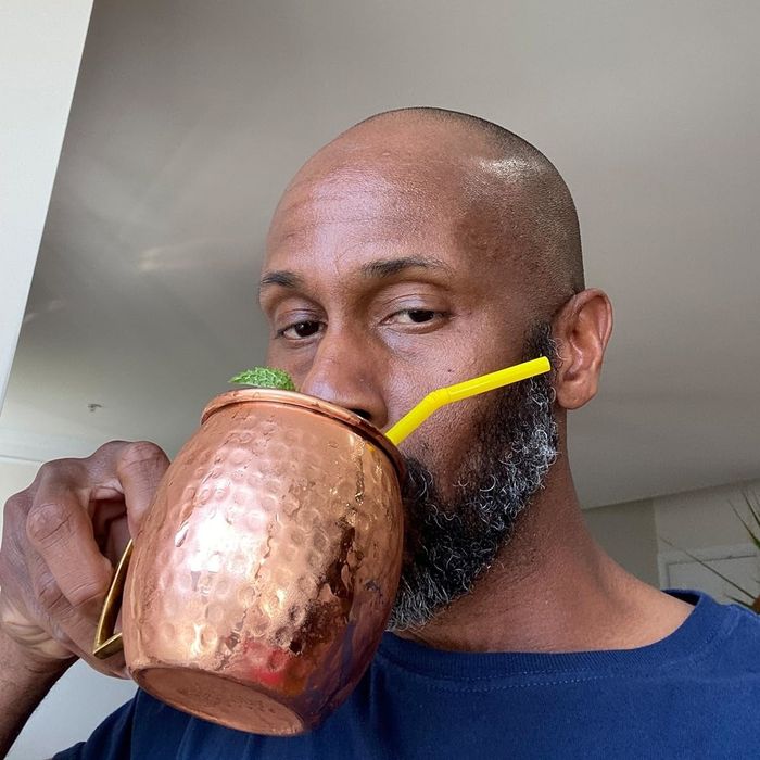 A man enjoying a drink from a copper mug with a yellow straw, possibly demonstrating kitchenware for a shopping feature