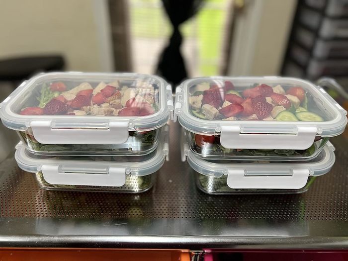 Four meal prep containers stacked and filled with an assortment of fruits and vegetables