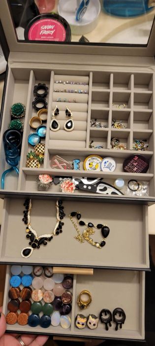 A jewelry organizer displaying an array of rings, earrings, necklaces, and pins, including beaded jewelry, quirky pins, and various types of rings