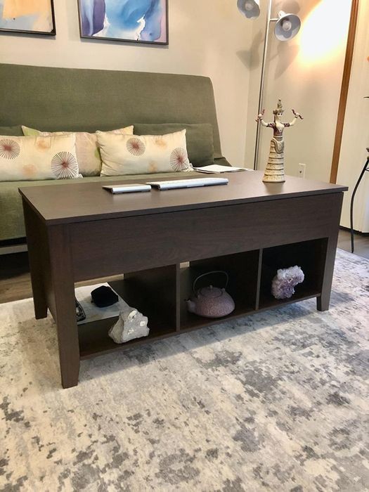 A reviewer's photo of a brown coffee table featuring three storage cubbies at the bottom