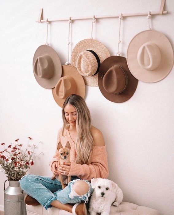 A model and two dogs posing beneath a hat rack displaying five wide-brimmed hats