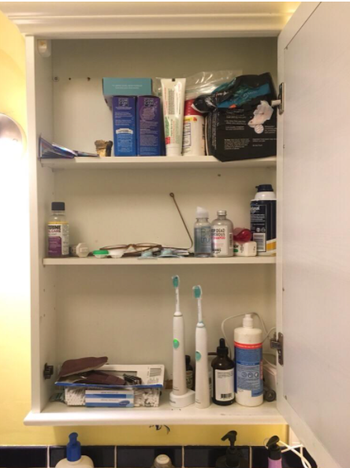 A reviewer's photo of their bathroom cabinet before installing the organizer