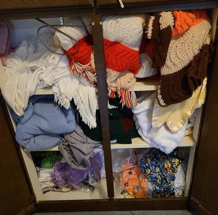 A closet shelf neatly arranged with folded knitted blankets and afghans in various patterns and textures, sorted by type