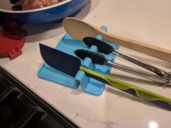 A spatula and tongs neatly placed on a bright blue silicone utensil rest