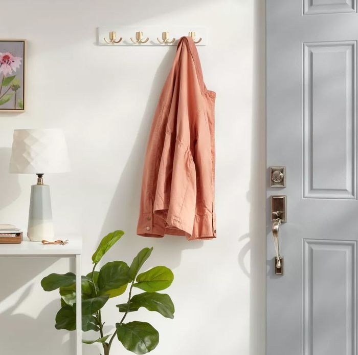 A jacket hanging on wall hooks in a neat entryway, complete with a lamp, plant, and a light-colored door.