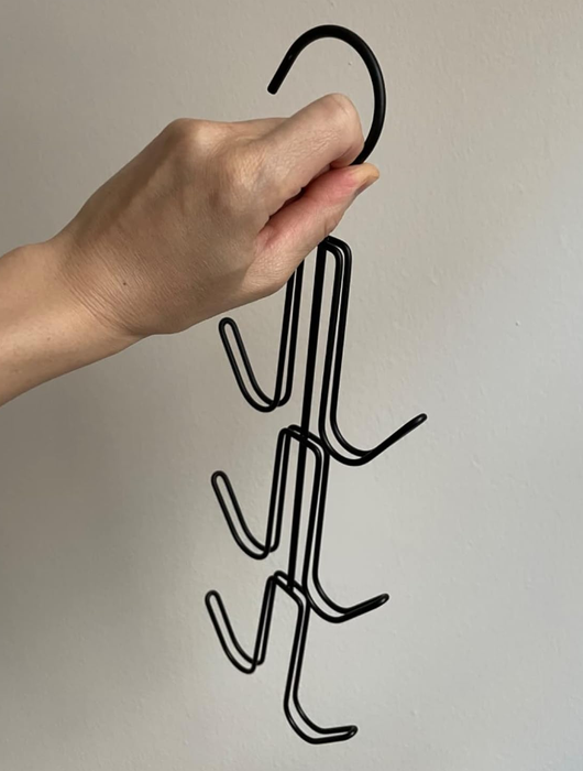 A hand holding a multi-tiered metal hanger equipped with hooks