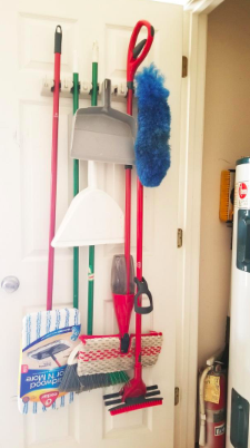 A reviewer's photo of a broom holder mounted on the inside of a closet door, neatly storing brooms and mops